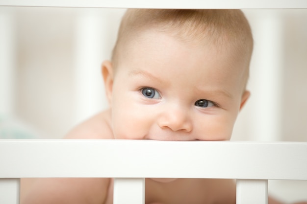 Adorable bebé mordiendo el tablero de su cuna de madera