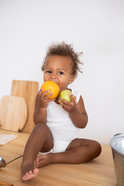 Adorable bebé negro sosteniendo algunas frutas