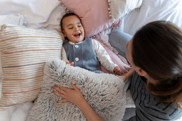 Adorable bebé riendo y jugando con su madre en la cama