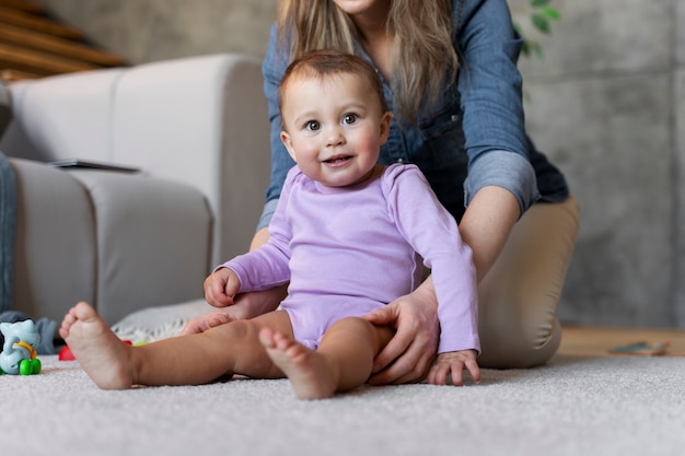 Adorable bebé sostenido por su madre y sentado en el suelo