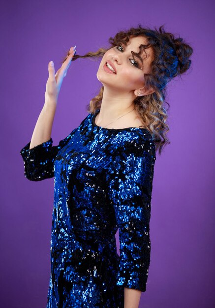 Adorable chica de pelo rizado estirando su cabello y de pie sobre fondo morado Foto de alta calidad