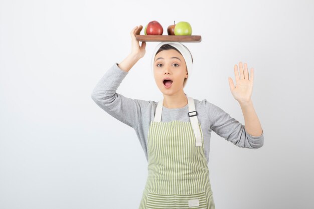 Adorable cocinera sosteniendo un plato de manzanas en blanco.