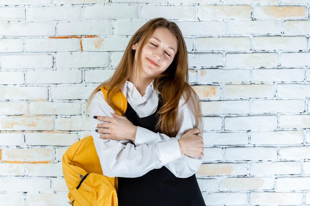 Adorable colegiala se encuentra en el fondo blanco y se siente feliz