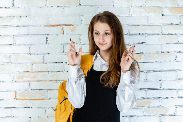 Adorable colegiala se para sobre fondo blanco y señala con el dedo hacia arriba