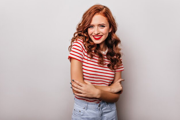 Adorable dama delgada en camiseta a rayas sonriendo. Atractiva pelirroja divirtiéndose