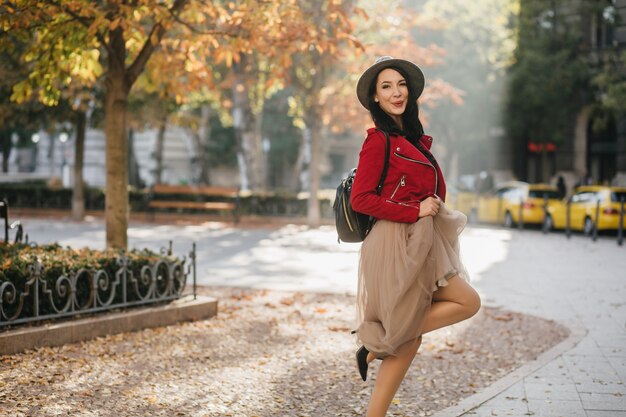 Adorable dama morena en falda larga bailando en el parque otoño