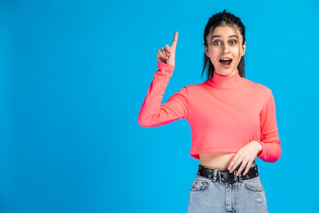 Adorable dulce niña de fondo azul levanta la mano y gesticula paz Foto de alta calidad