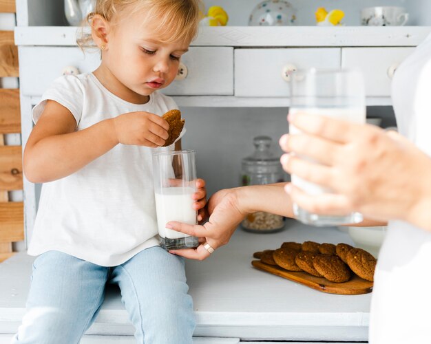 Adorable hija comiendo galletas con leche