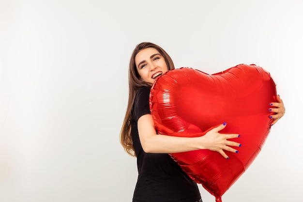 Adorable joven sosteniendo un globo rojo en forma de corazón y riendo