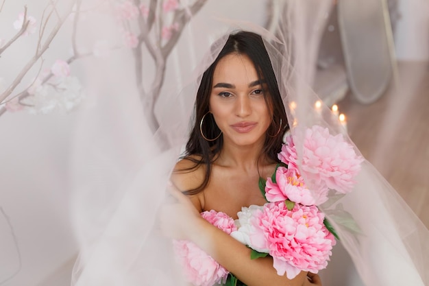 Adorable jovencita abrazando sus flores bajo el tul Foto de alta calidad