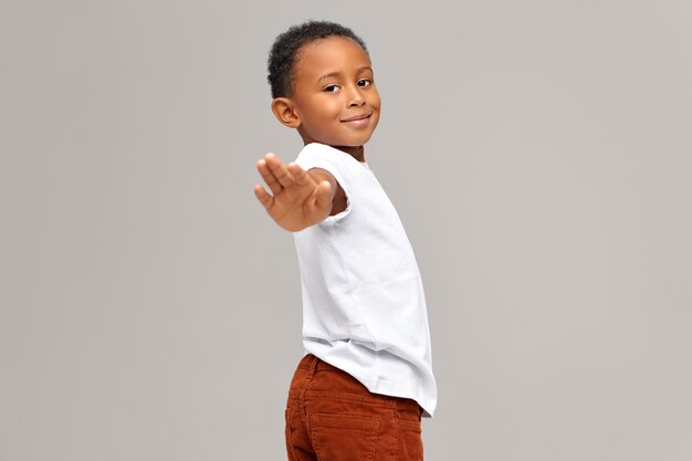 Adorable lindo niño de piel oscura extendiendo la mano haciendo gesto de parada o diciendo adiós. Hermoso niño afroamericano gesticulando, dando señal, enviando mensaje. Comunicación no verbal