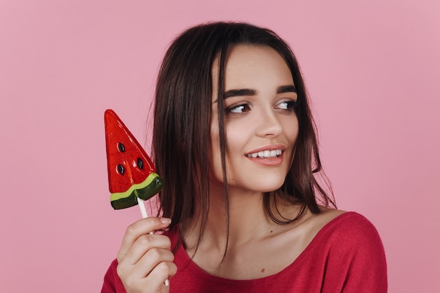 Adorable morena tiene una piruleta posando en la habitación rosa