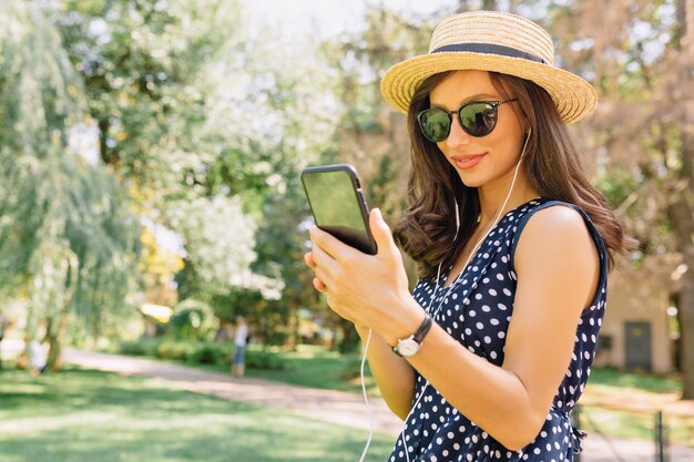 Adorable mujer alegre con smartphone y disfrutando de caminar en el parque