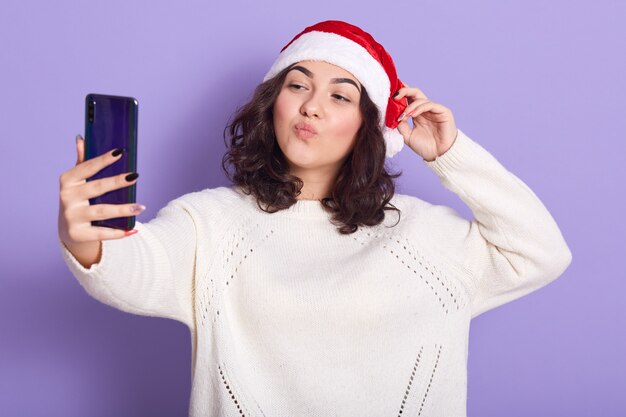 Adorable mujer bastante joven que pone una mano en el sombrero rojo de santa claus