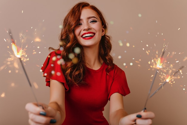 Adorable mujer blanca posando con luces de bengala. Hermosa chica pelirroja sosteniendo bengalas y riendo en año nuevo.