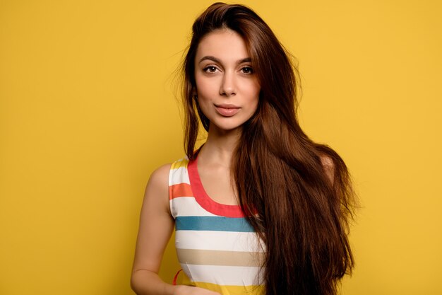 Adorable mujer de cabello oscuro, alegre dama caucásica aislada en la pared amarilla.