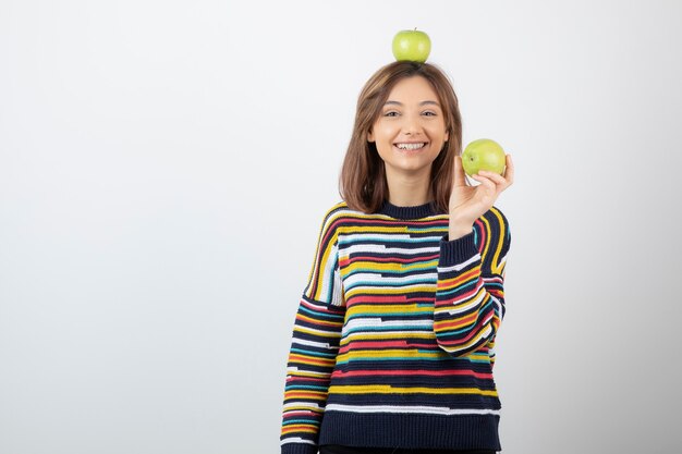 Adorable mujer joven en ropa casual con manzanas verdes sobre fondo blanco.