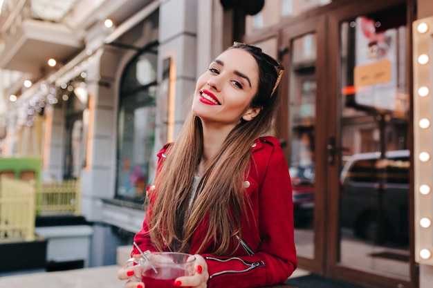 Adorable mujer con maquillaje de moda riendo mientras bebe té en el espacio de la calle