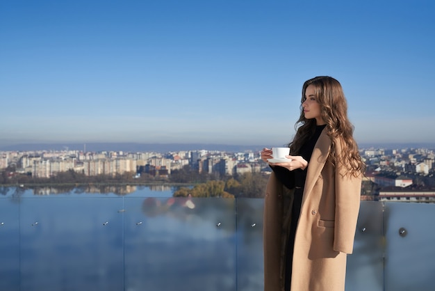 Adorable mujer de pie en el balcón con una taza de café