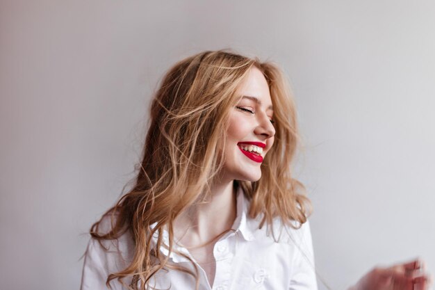 Adorable mujer rubia riendo con los ojos cerrados Foto de estudio de encantadora chica caucásica en camisa blanca