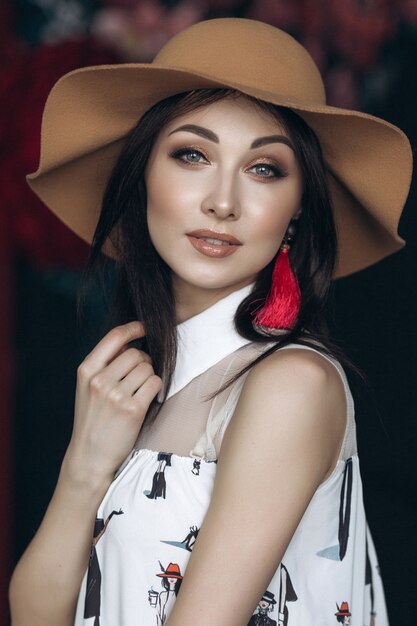 Adorable mujer sonriente en sombrero beige y con look de moda plantea en el estudio