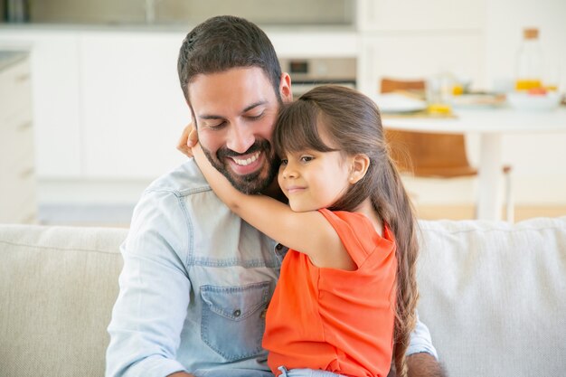 Adorable niña abrazando a su papá mientras está sentado en su regazo.