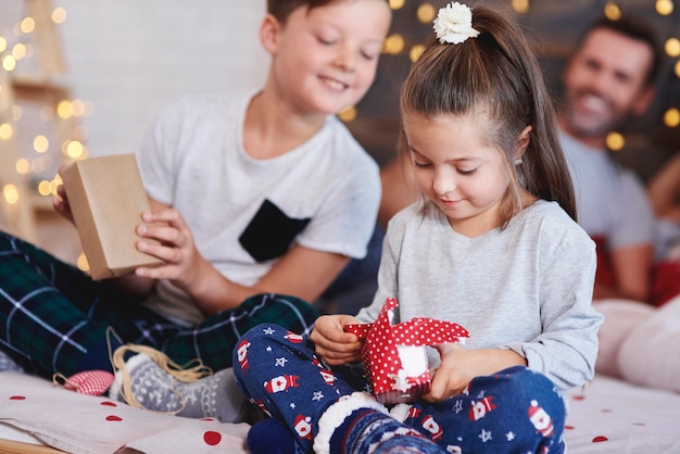 Adorable niña abriendo regalo de Navidad en la cama