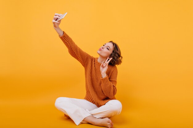 Adorable niña descalza tomando foto con el signo de la paz