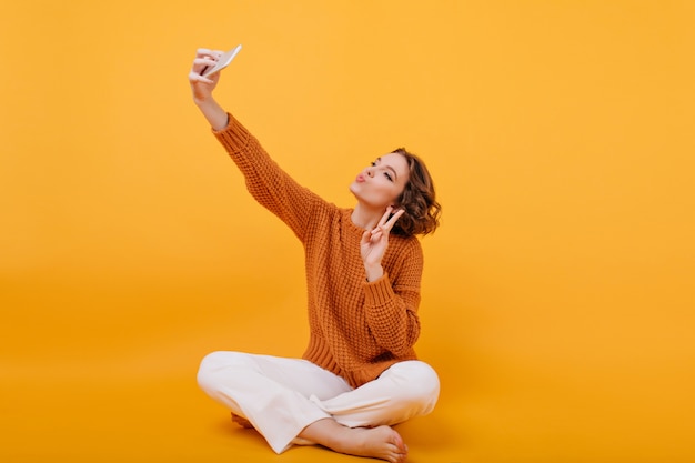 Adorable niña descalza tomando foto con el signo de la paz