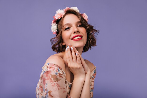 Adorable niña con hermosas flores en el cabello posando. Mujer blanca inspirada con sincera sonrisa de pie.