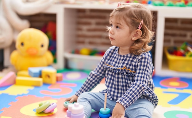 Adorable niña hispana jugando con aros sentados en el piso en el jardín de infantes