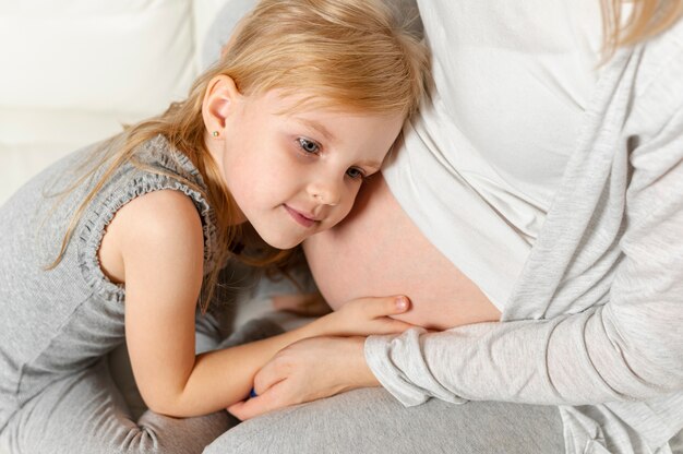 Adorable niña jugando con panza de madre embarazada