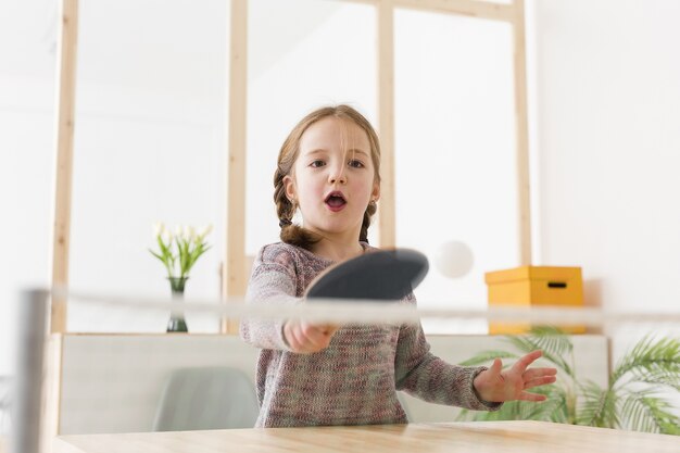 Adorable niña jugando tenis de mesa en el interior