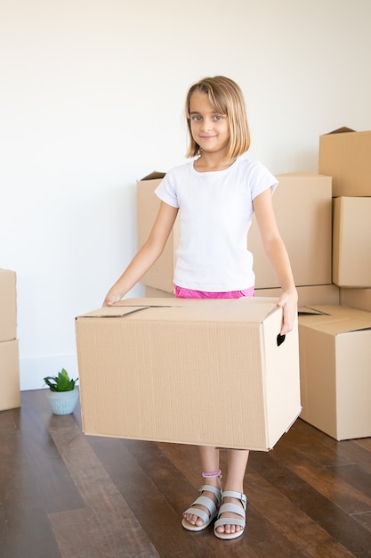 Adorable niña llevando caja de cartón y mirando a cámara