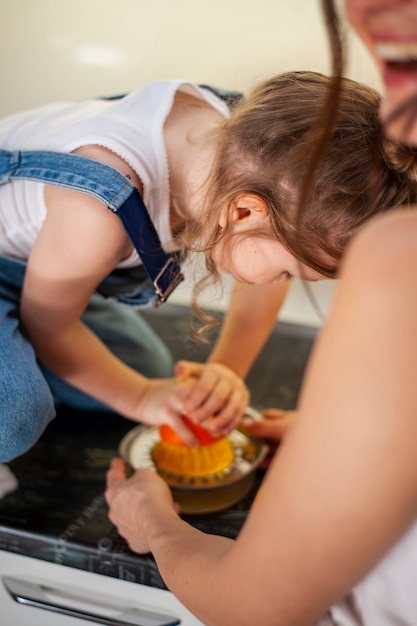 Adorable niña y madre preparando jugo de naranja