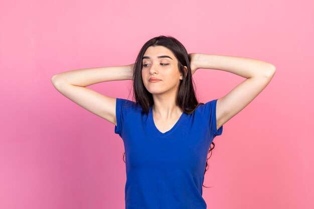 Adorable niña de pie sobre fondo rosa y sosteniendo sus manos detrás de su cabeza Foto de alta calidad