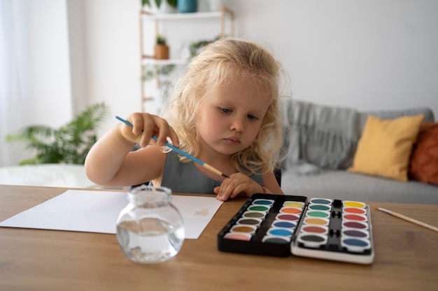 Adorable niña pintando sobre papel en casa