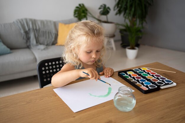 Adorable niña pintando sobre papel en casa