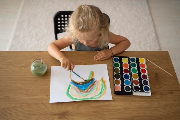 Adorable niña pintando sobre papel en casa