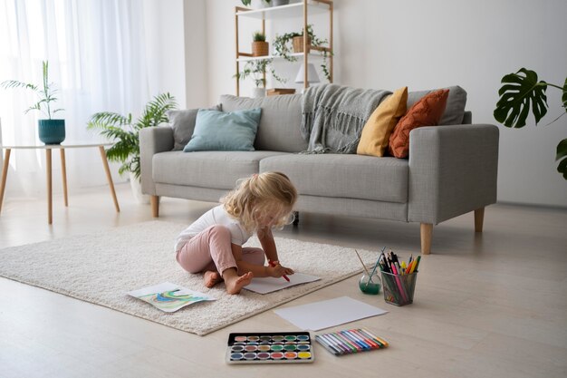 Adorable niña pintando sobre papel en casa