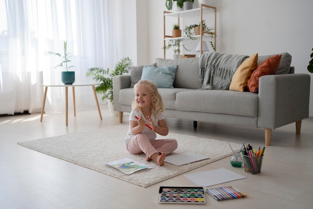 Adorable niña pintando sobre papel en casa