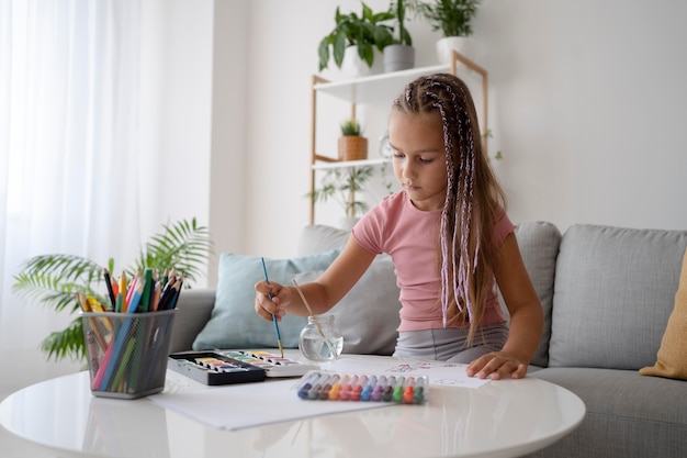 Adorable niña pintando sobre papel en casa