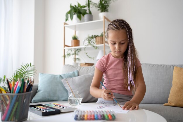 Adorable niña pintando sobre papel en casa