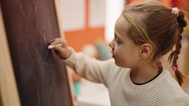 Adorable niña rubia estudiante de preescolar dibujando en la pizarra en el jardín de infantes