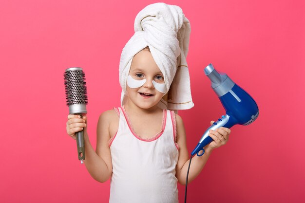 Adorable niña con secador de pelo y peine en las manos