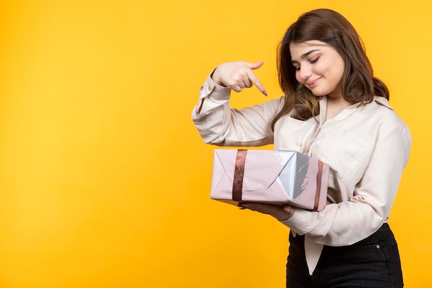 Adorable niña sosteniendo una caja de regalo rosa y apuntándolo con más precisión Foto de alta calidad