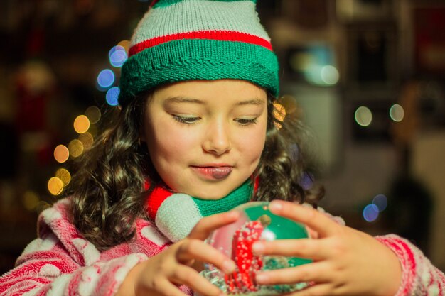 Adorable niña sosteniendo y mirando su bola de cristal de Navidad