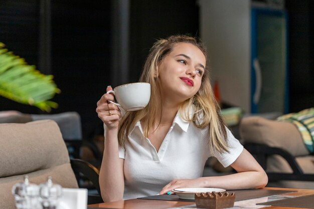 Adorable niña sosteniendo una taza de café y mirando a un lado