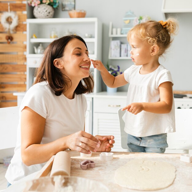 Adorable niña y su madre jugando con harina