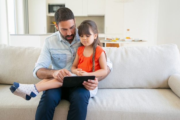 Adorable niña y su papá viendo la película en tableta juntos.